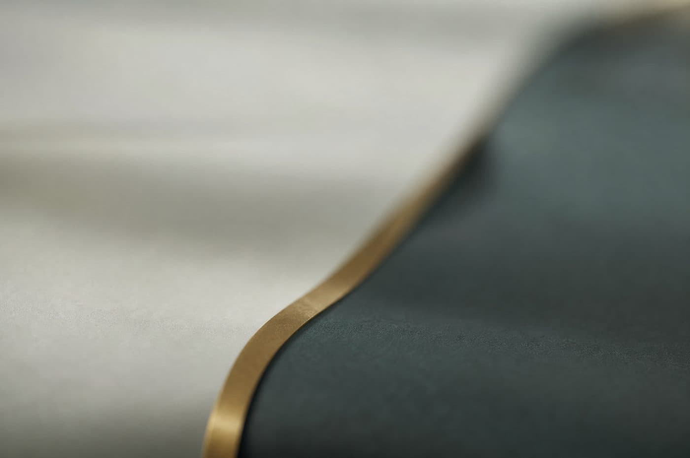 An out-of-focus field of pale grey and deep teal with a single brass curve running through it — nothing in it resolves.