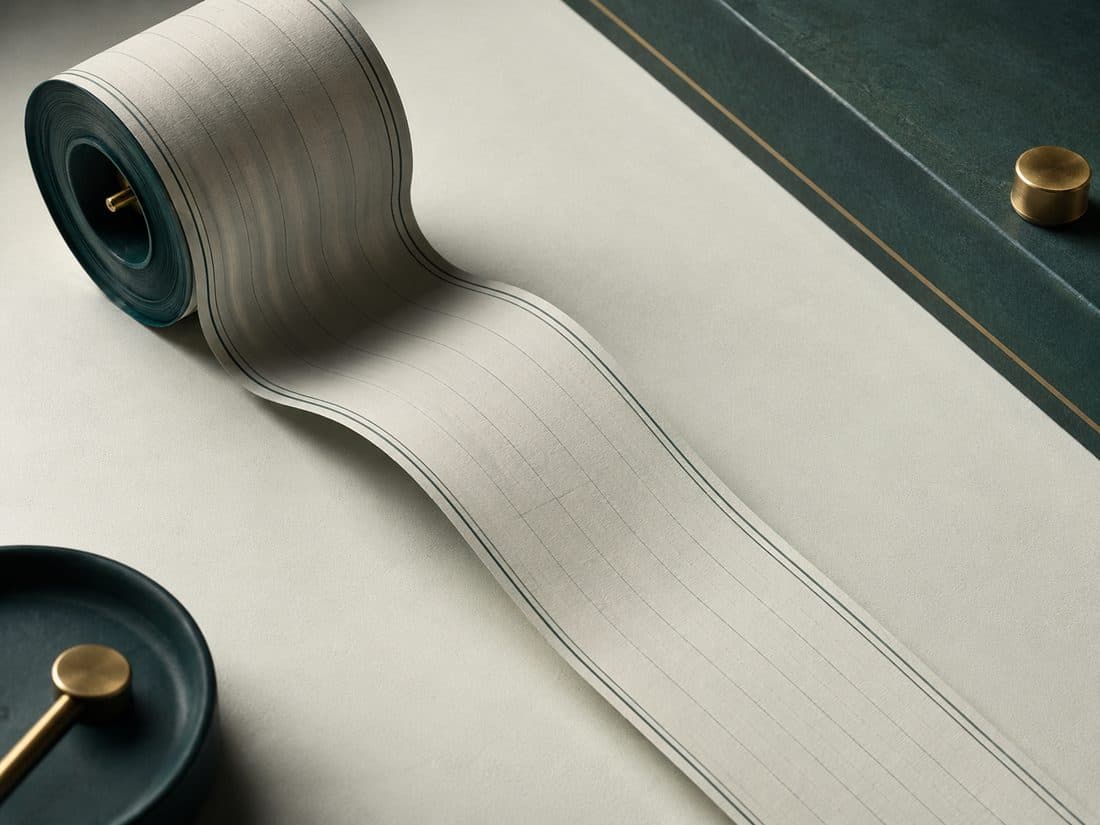 A long narrow tape unrolling and curling gently onto a pale surface, seen from above, with a shallow teal dish beside it.