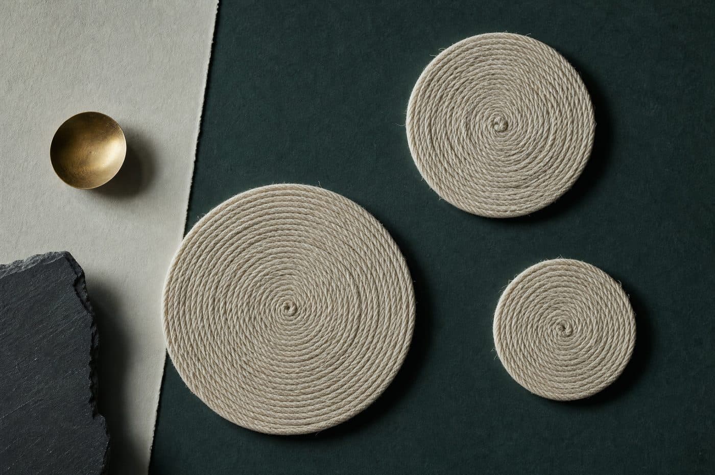 Three flat spiral coils of pale cord of different diameters, laid apart from one another beside a small brass weight.